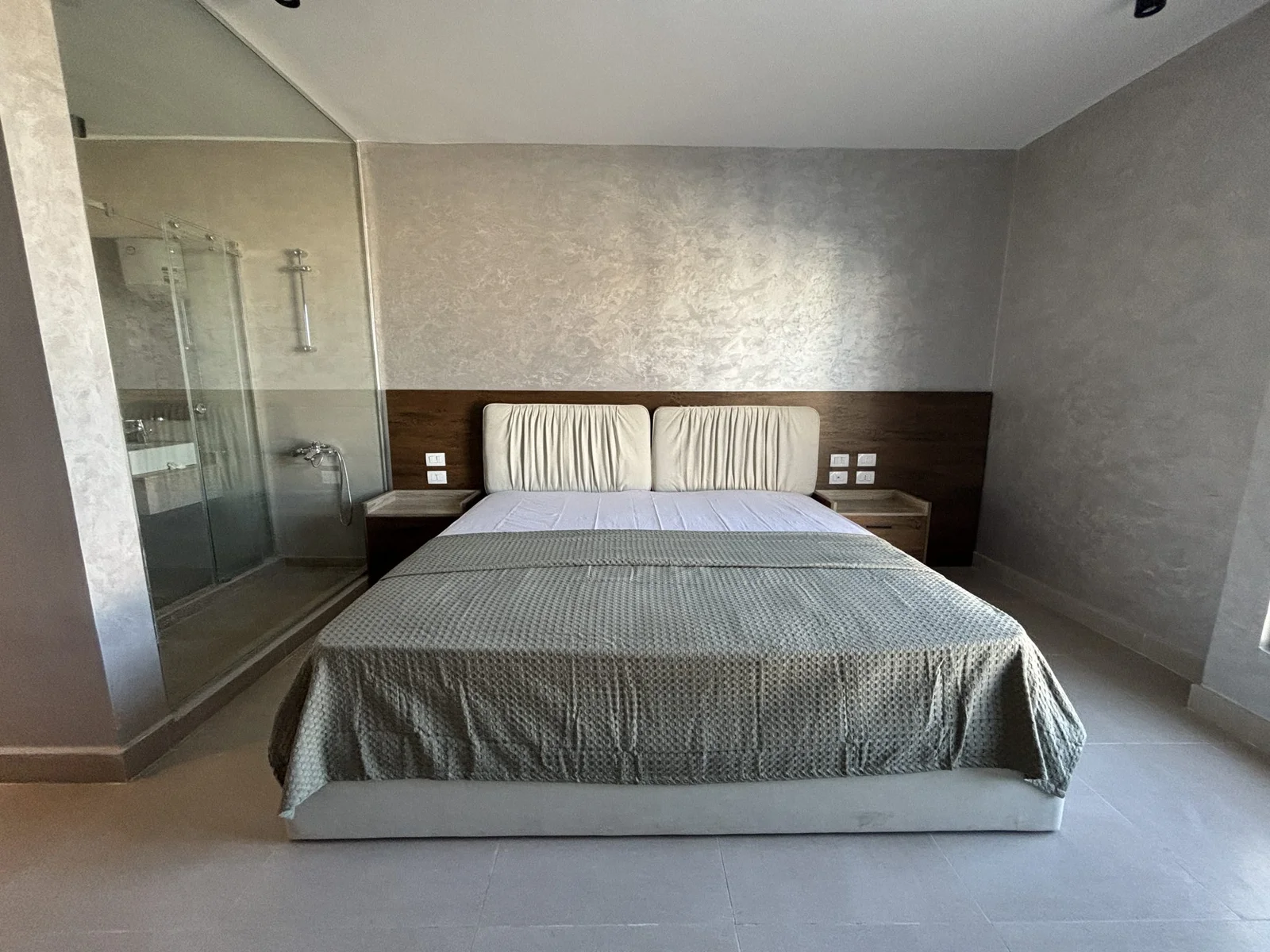 Holiday-home bedroom with wooden headboard, grey bedding and an en-suite glass shower
